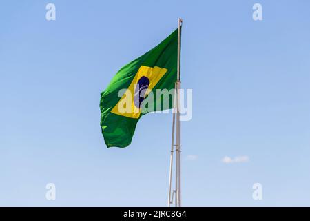 Goiânia, Goias, Brasilien – 23. August 2022: Die Flagge Brasiliens. Die Flagge Brasiliens fliegt, flattert im Wind und der blaue Himmel im Hintergrund. Stockfoto