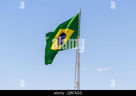Goiânia, Goias, Brasilien – 23. August 2022: Die Flagge Brasiliens. Die Flagge Brasiliens fliegt, flattert im Wind und der blaue Himmel im Hintergrund. Stockfoto