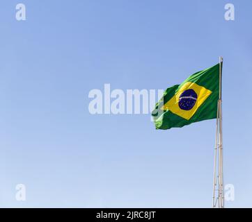Goiânia, Goias, Brasilien – 23. August 2022: Die Flagge Brasiliens. Die Flagge Brasiliens fliegt, flattert im Wind und der blaue Himmel im Hintergrund. Stockfoto