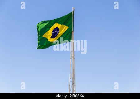 Goiânia, Goias, Brasilien – 23. August 2022: Die Flagge Brasiliens. Die Flagge Brasiliens fliegt, flattert im Wind und der blaue Himmel im Hintergrund. Stockfoto