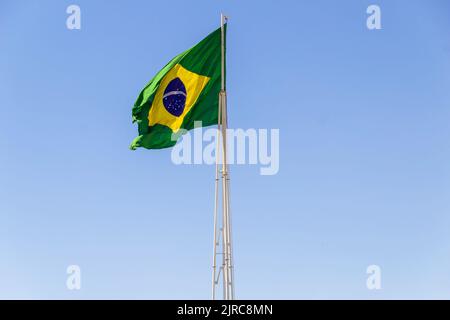 Goiânia, Goias, Brasilien – 23. August 2022: Die Flagge Brasiliens. Die Flagge Brasiliens fliegt, flattert im Wind und der blaue Himmel im Hintergrund. Stockfoto
