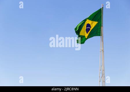 Goiânia, Goias, Brasilien – 23. August 2022: Die Flagge Brasiliens. Die Flagge Brasiliens fliegt, flattert im Wind und der blaue Himmel im Hintergrund. Stockfoto