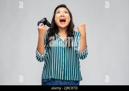 Glückliche asiatische Frau spielt Videospiel mit Gamepad Stockfoto