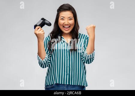 Glückliche asiatische Frau spielt Videospiel mit Gamepad Stockfoto
