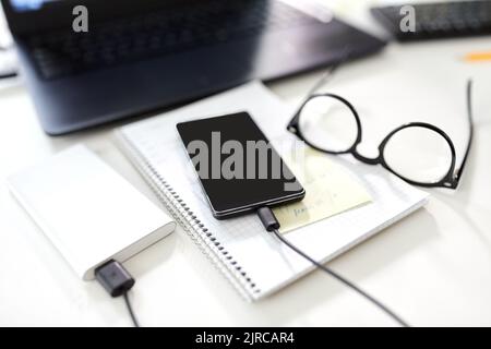 Smartphone mit Powerbank auf dem Tisch im Büro Stockfoto