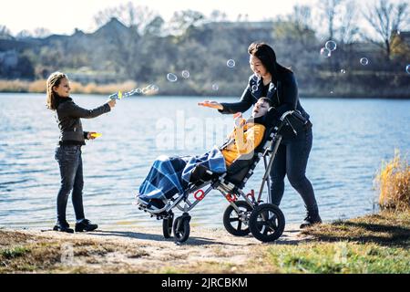 Glückliche Familie, Mutter, Tochter und Sohn mit zerebraler Lähmung verbringen gemeinsam Zeit am Flussufer. Stockfoto