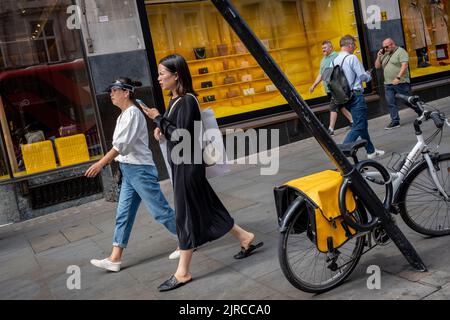 Die Käufer kommen am 23.. August 2022 in London, England, an einem schiefen Pfosten vorbei, wo vor der Regent Street-Filiale des legendären britischen Einzelhändlers Burberry ein Fahrrad gesperrt wurde. Stockfoto