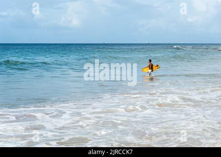 Ein Surfer, der gegen den blauen Himmel und weiße Wolken ins Meer eindringt. Salvador, Brasilien. Stockfoto