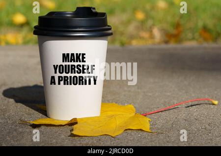 Auf einem gelben Ahornblatt gibt es eine Tasse Kaffee, auf dem geschrieben steht - machen Sie sich eine Priorität. Geschäftskonzept. Stockfoto