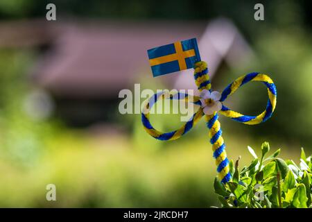 Eine kleine schwedische Flagge auf verschwommenem Hintergrund während der Mittsommerfeier Stockfoto