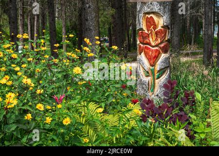 Eine Blumenholzschnitzerei auf einem Totempfahl in einem Blumengarten im Riding Mountain National Park, Manitoba, Kanada. Stockfoto