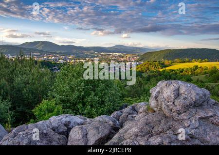 Der Sonnenuntergang über Banska Bystrica Stadt hinter Grün und Felsen umgeben von Bergen Stockfoto