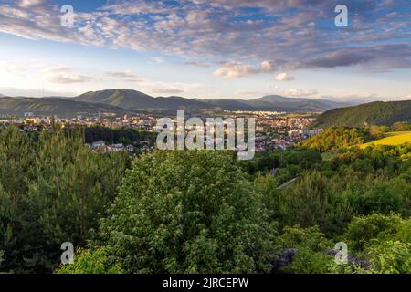 Der Sonnenuntergang über Banska Bystrica Stadt von hinter Grün umgeben von Bergen Stockfoto