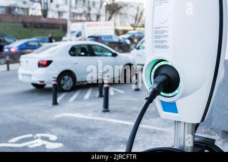 Elektroauto-Ladegerät aus der Nähe mit Autos im Hintergrund auf dem Parkplatz Stockfoto