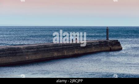 Ein Mann und eine Frau gehen Hunde auf einem Pier bei Sonnenuntergang in Cascais, Portugal Stockfoto
