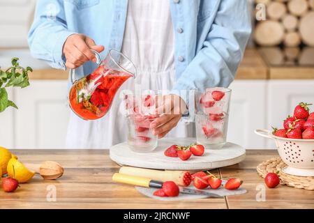 Frau goss leckere Erdbeerlimonade in Glas in der Küche Stockfoto
