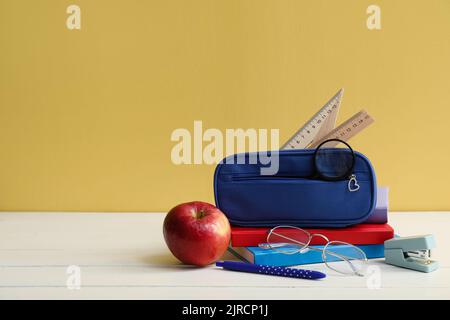 Bleistiftetui mit Schulpapiere, Brillen und Apfel auf Tisch vor gelbem Hintergrund Stockfoto