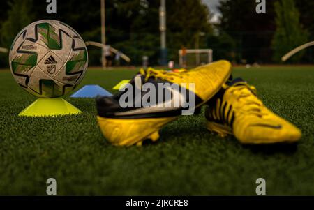 Eine Nahaufnahme eines gelben Nike CTR360 Maestri Fußballschubes und eines Adidas-Balls im Feld Stockfoto