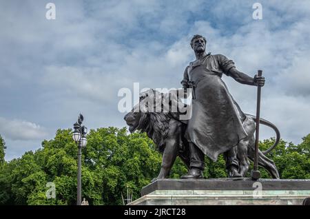 London, England, Großbritannien - 6. Juli 2022: Victoria Memorial. Nahaufnahme der Manufakturstatue mit Schmied mit Hammer und Schriftrolle. Löwe unter blauem Clou Stockfoto