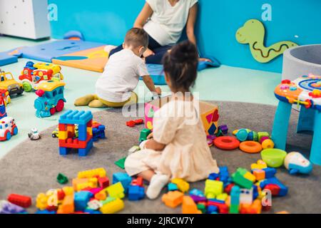 Kreative Spielzeit im Kindergarten. Kleinkinder spielen mit Plastikbausteinen, bunten Autos und anderen Spielsachen, während sie auf dem Boden sitzen. Entwicklung von Feinmotorik und Bruttomotorik. Hochwertige Fotos Stockfoto