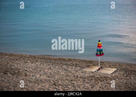 Einsamer Sonnenschirm am leeren Strand am Morgen, der auf den Sonnenaufgang wartet. Ruhiges blaues Meer. Calkidiki, Griechenland Stockfoto