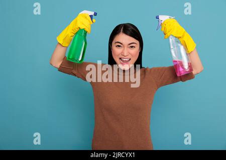 Glücklich aufgeregt und lächelnd asiatische Hausfrau heben die Arme und zeigt Bizeps isoliert blauen Hintergrund, Hausfrau Arbeiter, Reinigung Haus Konzept, positive Frau energiegeladen fröhlich und fröhlich Stockfoto