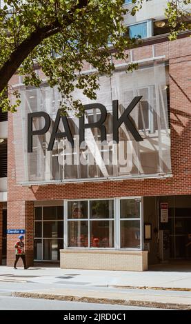 Dies ist die Vorderseite eines Parkhauses in York, PA, mit einem großen Schild mit der Aufschrift „PARK“ auf der Vorderseite des Gebäudes. Da ist eine Person, die draußen läuft. Stockfoto