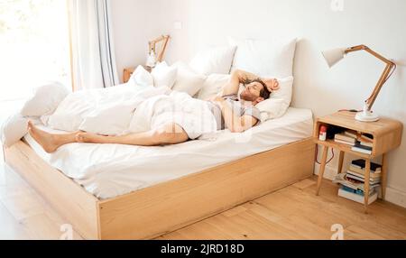 Entspannter Mann, der zu Hause im Bett schläft, müde Person, die im Schlafzimmer träumt und sich im Urlaub im Haus ausruht. Erschöpfter Mann, der sich im Hotel entspannt und schaut Stockfoto