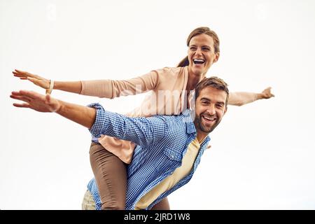 Genießen Sie unsere Freiheit. Ein Mann huckepack seine Freundin während des Tages im Freien. Stockfoto