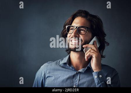 Ich rufe in Bezug auf deine Werbeanzeige an. Studio-Aufnahme eines hübschen jungen Mannes, der auf seinem Handy spricht, während er vor einem grauen Hintergrund steht. Stockfoto