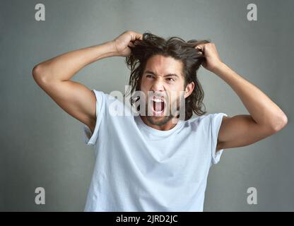 Hes kochte vor Wut über. Studioaufnahme eines jungen Mannes, der vor grauem Hintergrund schreit. Stockfoto