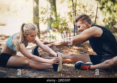 Paare, die zusammen trainieren, bleiben zusammen. Ein junges Paar, das sich gemeinsam im Freien ausdehnt. Stockfoto