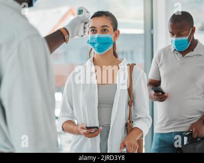 Einhaltung von Vorschriften, Reisebeschränkungen und behördlicher Auflagen durch Sicherheitsscannen der Temperatur von Touristen mit einem Infrarot-Thermometer am Flughafen. Arbeiterkontrolle oder Fieber Stockfoto