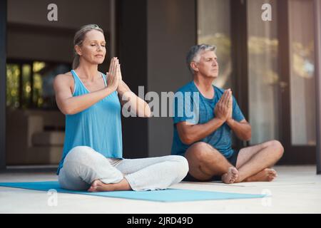 Friedliche Geister sind glückliche Geister. Ein reifes Paar tritt friedlich in eine Yoga-Pose mit gekreuzten Beinen und zusammengesteppten Händen ein. Stockfoto