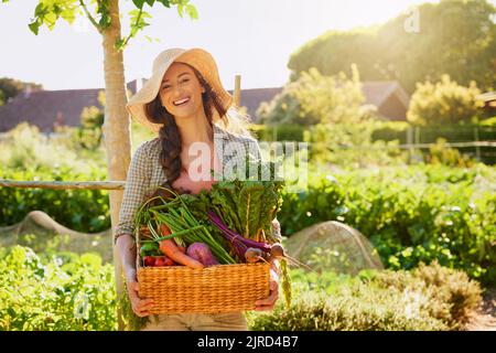 Von Mutter Natur selbst gewachsen. Porträt einer jungen Frau, die einen Korb mit frisch gepflückten Produkten in einem Garten trägt. Stockfoto