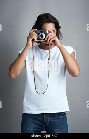 Ein Klick, viele Erinnerungen. Studioportrait eines jungen Mannes, der mit einer Vintage-Kamera vor einem grauen Hintergrund posiert. Stockfoto