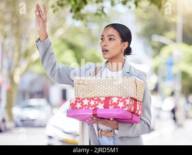 Frau, die ein Geschenk hält und auf der Straße ein Taxi für die Reise zu einem Geburtstag, Jubiläum oder einer Gratulationsfeier anruft. Stadtmädchen steht auf der Straße Stockfoto