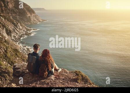Machen Sie eine Pause, um die Aussicht zu genießen. Hochwinkelaufnahme eines liebevollen jungen Paares, das den Blick von einem Berggipfel aus betrachtet. Stockfoto