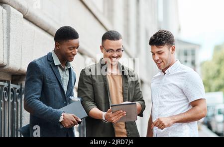 Informelle Gruppe von IT-Ingenieuren, die sich gemeinsam auf ein Meeting auf einem digitalen Tablet draußen vorbereiten. Ein vielseitiges Team von glücklichen Technikern, die Pläne sprechen und lesen Stockfoto