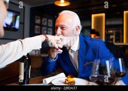Eleganter älterer Mann, der die Hand seiner Frau küsst Stockfoto
