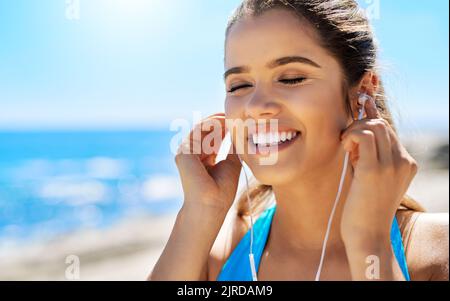 Musik macht Lust auf Bewegung. Eine junge Frau, die Musik hört, während sie am Meer läuft. Stockfoto