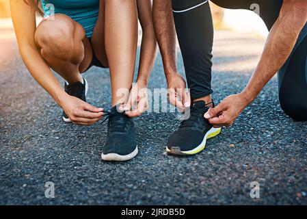 Ein unbekanntes junges Paar schnürt ihre Schnürsenkel, während es unterwegs ist. Stockfoto