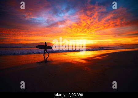 Eine Silhouette von Surfern, die am Abend entlang der Küste spazieren. Langzeitaufnahme des Sonnenuntergangs über der Halbinsel Nosara, Costa Rica Stockfoto