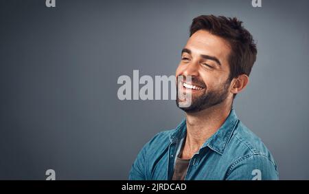 Lachen trägt so viel zum Tag bei. Studioaufnahme eines hübschen und glücklichen jungen Mannes, der vor grauem Hintergrund posiert. Stockfoto