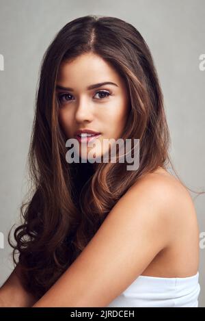 Shes eine atemberaubende Schönheit. Studioaufnahme einer jungen schönen Frau mit langen wunderschönen Haaren, die vor einem grauen Hintergrund posiert. Stockfoto