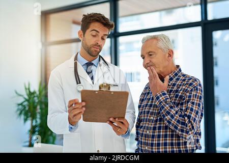 Ich mache mir ein wenig Sorgen um Ihre Testergebnisse. Ein Arzt und sein reifer Patient betrachten die Testergebnisse in einem Clipboard im Krankenhaus. Stockfoto