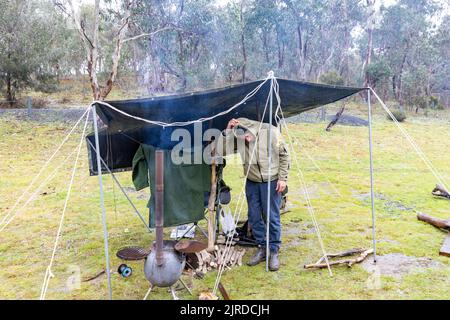 Mann, der im regionalen New South Wales zelte, stand unter einer Plane, um sich in Auspig, Australien, trocken zu halten und sich durch Feuer warm zu halten Stockfoto