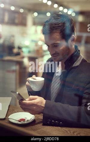 Ich schnappte mir schnell einen Kaffee. Ein hübscher junger Mann benutzte sein Handy, während er in einem Café saß. Stockfoto