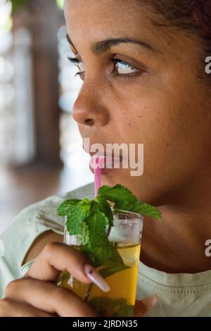 Eine 22-jährige Kubanerin, die ihren Mojito-Cocktail schlürft, Varadero Beach, Kuba. Stockfoto