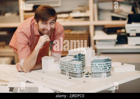 Junge Erwachsene kaukasische Architekt, der am Tisch mit Projekt, Zeichnungen und Bauplan im Architekturbüro arbeitet. Stockfoto